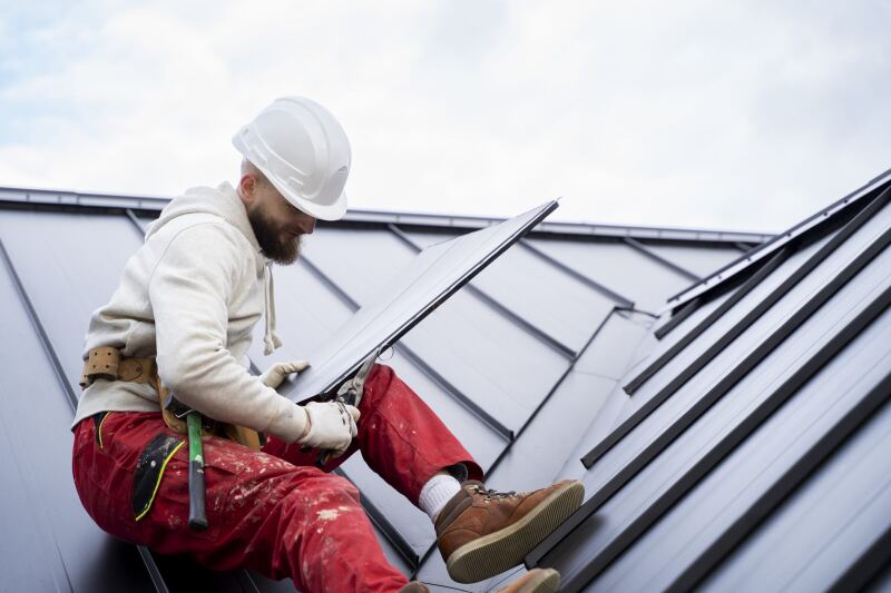 A roofer trimming a standing-seam metal sheet to fit against the ridge
